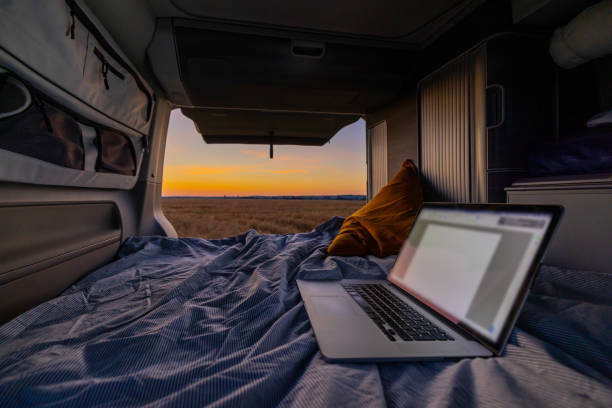 istock Laptop on bedding inside van parked on field during sunset 1414607381
