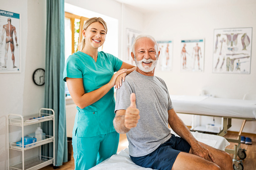 Attractive young female physiotherapist posing with a senior male patient