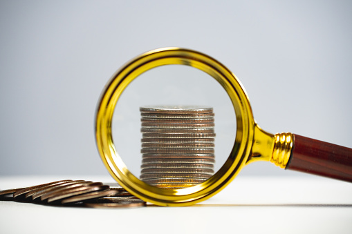 A stack of coins under a magnifying glass. Review of capital and investments. Business model for capitalization