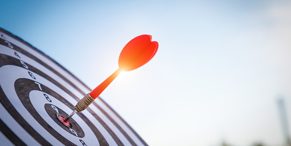 Close up shot red darts arrows in the target  of dartboard center on dark blue sky background. Business target or goal success and winner concept.