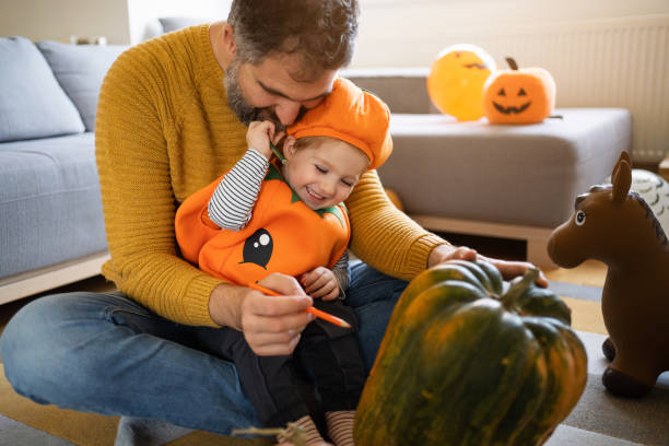ojciec i mały chłopiec przebrani za dynię, na halloween rysując razem na dyni - house halloween autumn candid zdjęcia i obrazy z banku zdjęć