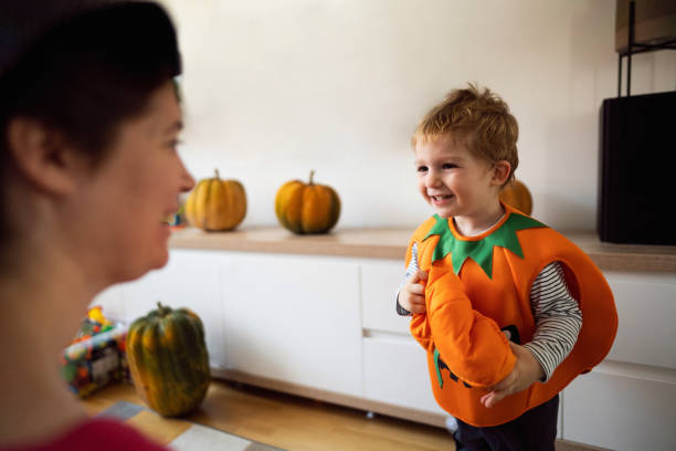 Toddler boy dressed as a pumpkin, for a Halloween showing his costume to mother