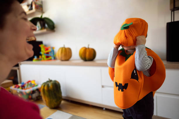 Toddler boy dressed as a pumpkin, for a Halloween showing his costume to mother