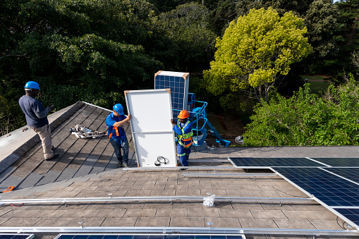Team of blue collar workers installing solar panel on roof of building