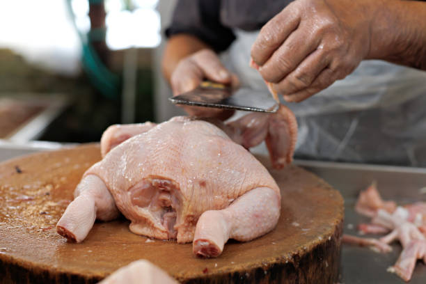 Cropped image of an Asian butcher chopping raw chicken meat at market stall