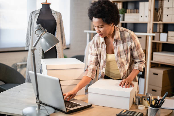 istock Young smiling entrepreneur woman working in her small workshop packing a merchandise to send it to online buyers. 1414624836
