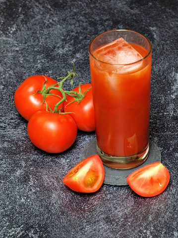 A glass of tomato juice with ice and tomatoes isolated on dark background.