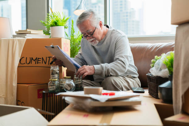asian elder senior man thinking calculate rental and mortgage rate while finish packing all stuff home moving ,concentrate financial home calculate with old white beadr grey hair male sit on sofa write down all debt in housing boom concept anciano asiático hombre mayor pensando en calcular el alquiler y la tasa hipotecaria mientras termina de empacar todas las cosas mudanza de la casa, concentrar la casa financiera calcular con el viejo abalorio blanco cabello gris hombre sentado en el sof�
