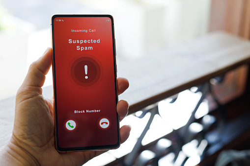 A man receiving an incoming suspected spam call on her phone. The network provider detect the scam and show warning sign to rejects the call.