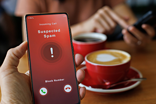 A man receiving an incoming suspected spam call on his phone. The network provider detect the scam and show warning sign to rejects the call.