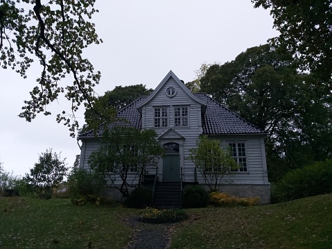 Traditional and old house in norway, bergen. Old and abandoned white wooden house with a garden of natural green grass.