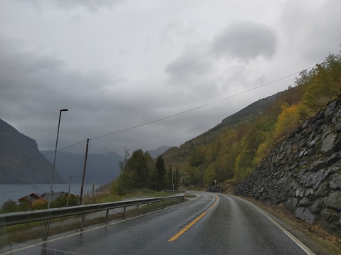 Wet roads with wet asphalt on a rainy day of travel in Norway direction Flam. Wet and humid conventional roads with mountains around that have waterfalls. Lots of greenery and nature.