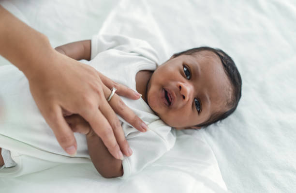 かわいいアフリカ系アメリカ人の新生児がベッドに横たわり、寝室でカメラを見ているクローズアップポートレート。母親の手は小さな子供を眠りに誘う。育児、黒人家族、新生児の男の子� - newborn baby african ethnicity little girls ストックフォトと画像