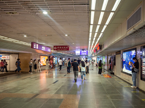 Xi'an, China - July 28, 2022: People walking along an underground passage.  A woman is standing by a corner of the passage operating a mobile device.