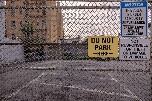 Long Island City, Queens, New York, NY, USA - July 5th 2022: Empty asphalt parking lot behind a solid wire fence and with poster telling not to park