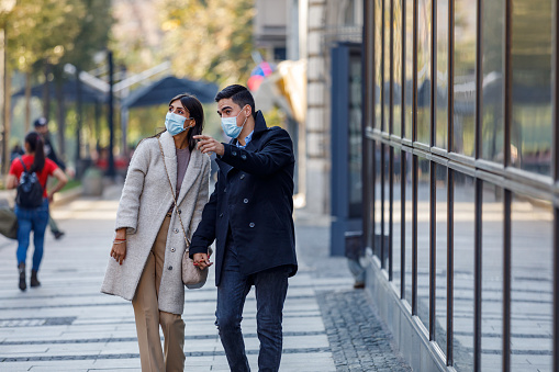 A modern couple wearing protective face masks is enjoying the nice weather and taking a look around the city.