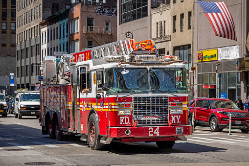 Midtown Manhattan, New York, NY, USA - July 5th 2022:  New York firetruck with a ladder on top driving up 6th Avenue with an American flag on a façade