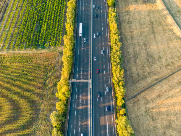 istock Highway from a bird's eye view. As the sun goes down, the sun's rays create beautiful long shadows on the ground. Yellow trees and surrounding farmland 1414639688