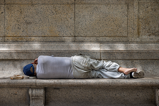 Bryant Park, Midtown Manhattan, New York, NY, USA - July 5th 2022: African-American man sleeping on a stone bench in front of the public library