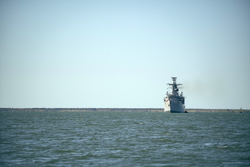 Grey modern warship sailing in still water.