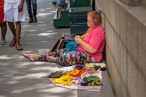 Bryant Park, Midtown Manhattan, New York, NY, USA - July 5th 2022: Woman sitting on the sidewalk outside Bryant Park and trying to sell knitwear