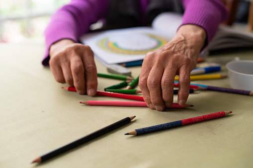 Hands of an elderly Latina from Bogota Colombia between 70 and 74 years old, coloring her mantras while at home