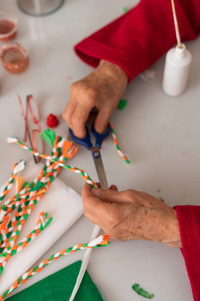 Hands of an elderly Latina from Bogota Colombia between 70 and 74 years old, making a craft with materials in her living room