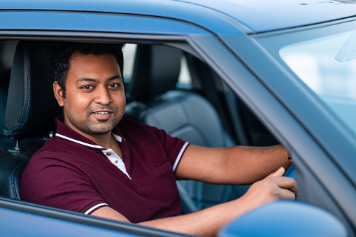 Outdoor image of attractive happy young man driving car and smiling.