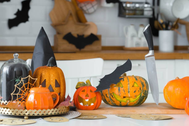 joyeux halloween! pumpkin jack sur la table. lanterne avec un sourire sculpté et différents attributs de la fête sur un fond clair à l’intérieur. pour des vacances en famille à la maison. espace de copie. - jack fruit photos et images de collection