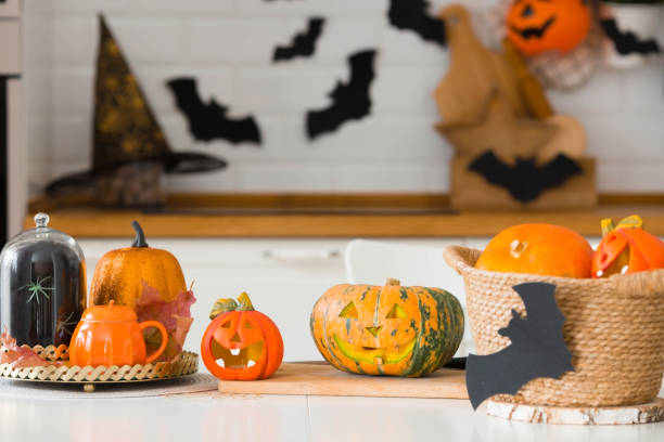 happy halloween! pumpkin jack on the table. lantern with a carved smile and different attributes of the holiday on a light background in the interior. for family holidays at home. copyspace. - jack fruit imagens e fotografias de stock