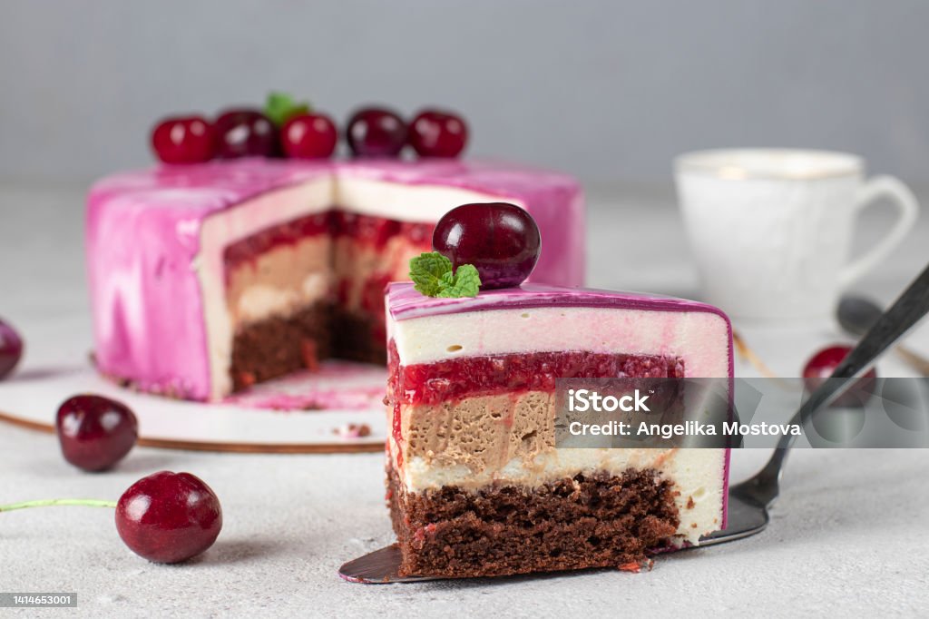 Piece of mousse cake with chocolate biscuit, vanilla and cream mousse, cherry confit and milk chocolate ganache Piece of mousse cake with chocolate biscuit, vanilla and cream mousse, cherry confit and milk chocolate ganache on gray background Almond Stock Photo