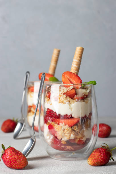 Layered strawberry dessert Trifle with biscuit, mascarpone cheese, almonds and shortbread tubes. Delicious dessert for kids party on light gray background stock photo