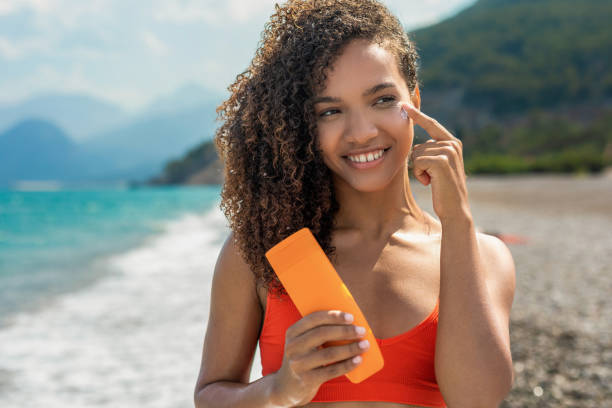 Smiling woman is applying suntan lotion on her face