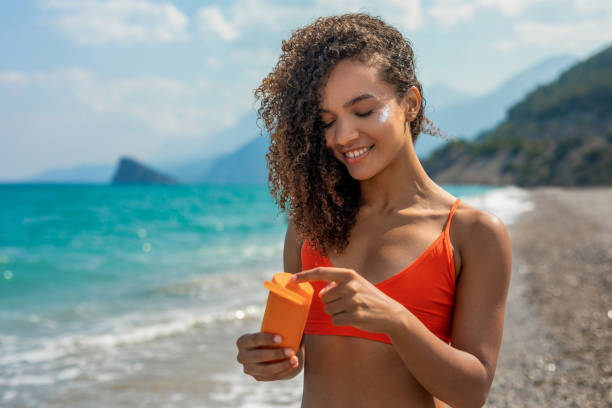 uśmiechnięta kobieta nakłada balsam do opalania na twarz - enjoyment people beach sun protection zdjęcia i obrazy z banku zdjęć