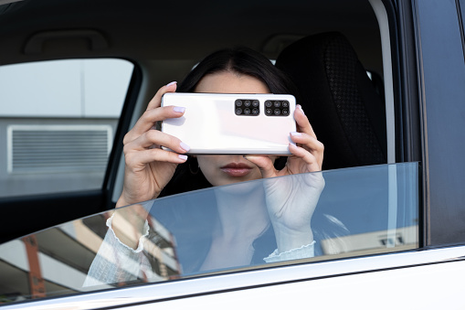 young woman takes pictures on the mobile phone from the car side window. a lot of cameras on smartphone. Spying with humor concept