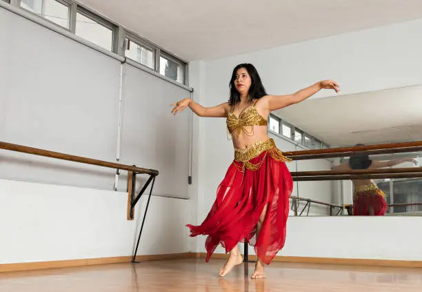 Photo of young belly dancer dressed in a red and gold costume dancing in a dance studio