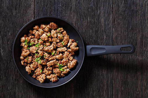 fried Italian sausage of freshly ground pork meat and spices in skillet on dark wooden table, horizontal view  from above, flat lay
