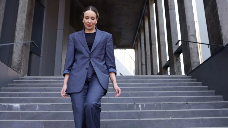 Young beautiful businesswoman go down the stairs. Girl walk on high heels against office building. Summer sunny day Outdoor