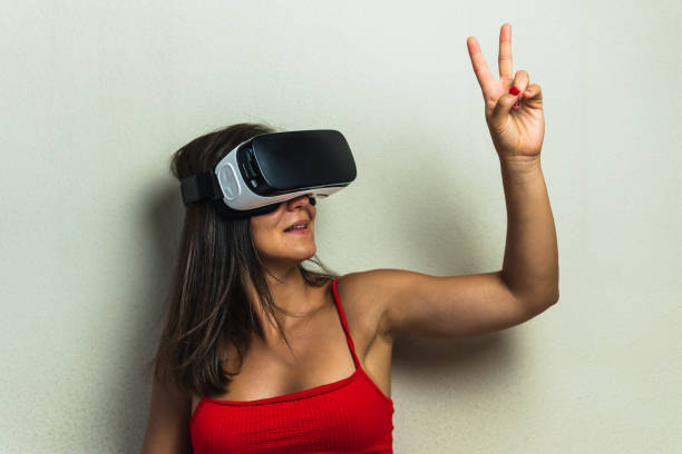 woman with virtual reality glasses raising two fingers upwards in victory sign. young girl in her room trying out augmented reality in three dimensions. - ai finger gamer imagens e fotografias de stock