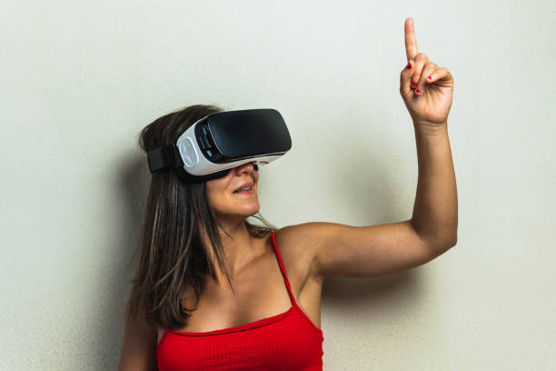 woman with virtual reality glasses pointing or raising a finger upwards. young girl in her room trying out augmented reality in three dimensions. - ai finger gamer imagens e fotografias de stock