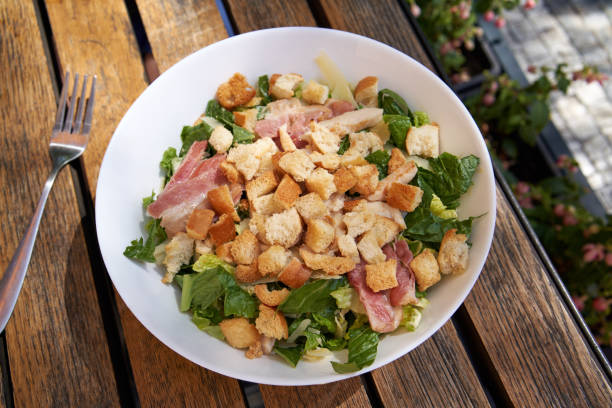 istock Caesar salad with croutons, bacon, lettuce and chicken in a restaurant, top view 1414674243