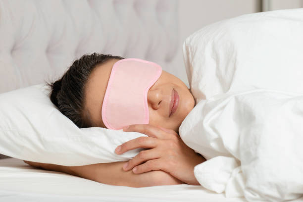 Sleeping Sleeping caucasian female with pink eye mask and a warm smile in white bed. sleep eye mask stock pictures, royalty-free photos & images