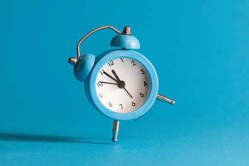 Blue alarm clock  in front of blue  wall. The clocks time is showing 5 to 12.