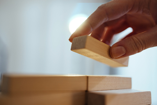 Close up photo of woman hand arranging wooden block stacking as step stair on a desk.