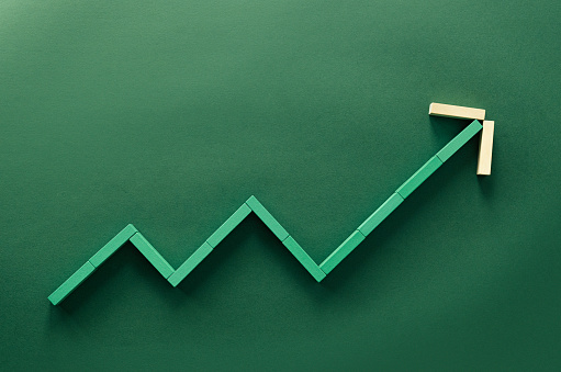 Close up photo of wooden block stacked in the shape of growing graph on green background.