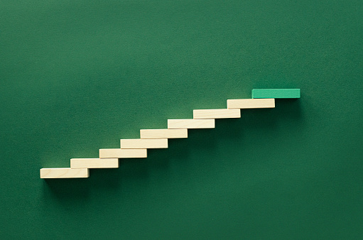 Close up photo of wooden block stacked in the shape of growing graph on green background.