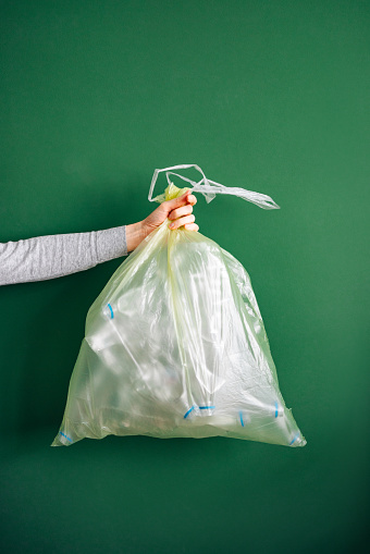 Close up photo of woman hand holding trash bag with plastic against green background.
