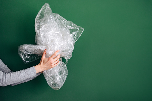 Close up photo of woman hands holding and recycling plastic against green background.