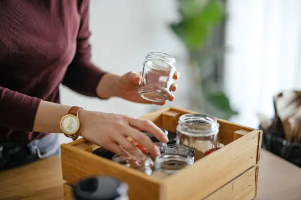 Close up photo of woman hands separates empty jars in a wooden crate at kitchen desk.