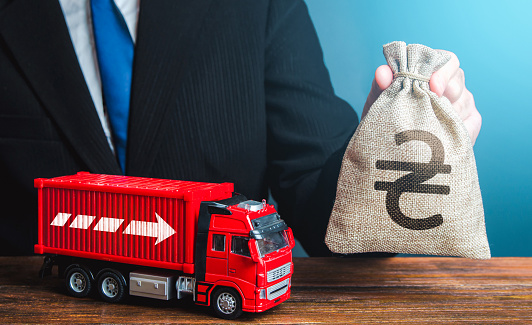 Businessman with ukrainian hryvnia money bag and truck. Income of the transport business and transport of goods. High salaries for drivers. Rising prices, global containers shortage crisis. Logistics